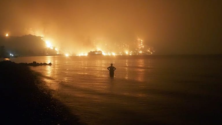 Ein Mann beobachtet, wie sich Waldbrände dem Strand von Kochyli in der Nähe des Dorfes Limni auf der Insel Evia (Griechenland) nähern.