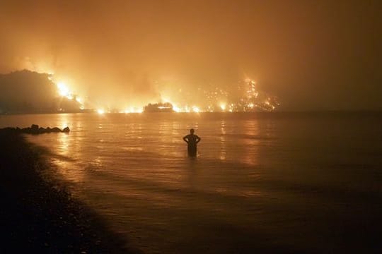 Ein Mann beobachtet, wie sich Waldbrände dem Strand von Kochyli in der Nähe des Dorfes Limni auf der Insel Evia (Griechenland) nähern.