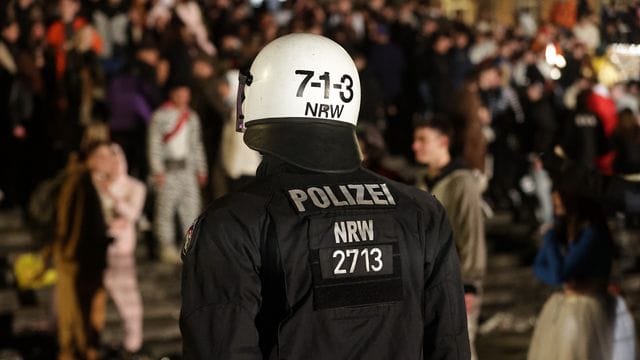 Ein Polizist beobachtet Feiernde beim Karneval in Düsseldorf (Archivbild): Ermittler suchen nun nach mindestens zwei Verdächtigen. Ein Polizist beobachtet Feiernde beim Karneval in Düsseldorf (Archivbild): Ermittler suchen nun nach mindestens zwei Verdächtigen.