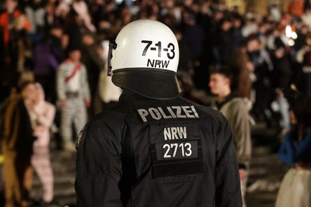 Ein Polizist beobachtet Feiernde beim Karneval in Düsseldorf (Archivbild): Ermittler suchen nun nach mindestens zwei Verdächtigen.