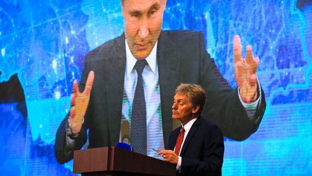 Wladimir Putin spricht bei einer Pressekonferenz per Video zu Medienvertretern, Kremlsprecher Dmitri Peskow hört zu.