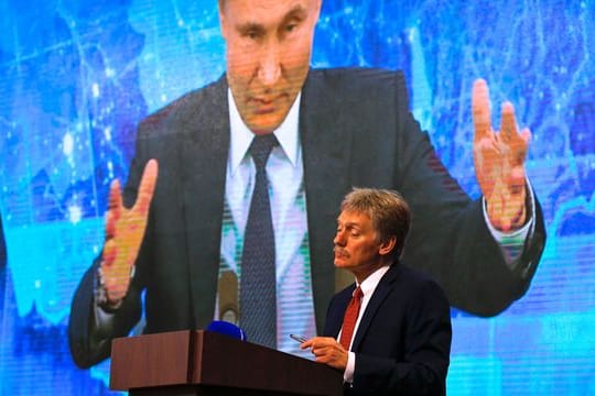 Wladimir Putin spricht bei einer Pressekonferenz per Video zu Medienvertretern, Kremlsprecher Dmitri Peskow hört zu.