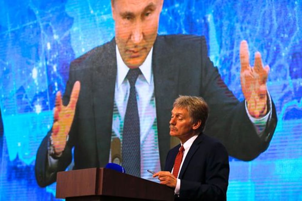 Wladimir Putin spricht bei einer Pressekonferenz per Video zu Medienvertretern, Kremlsprecher Dmitri Peskow hört zu.