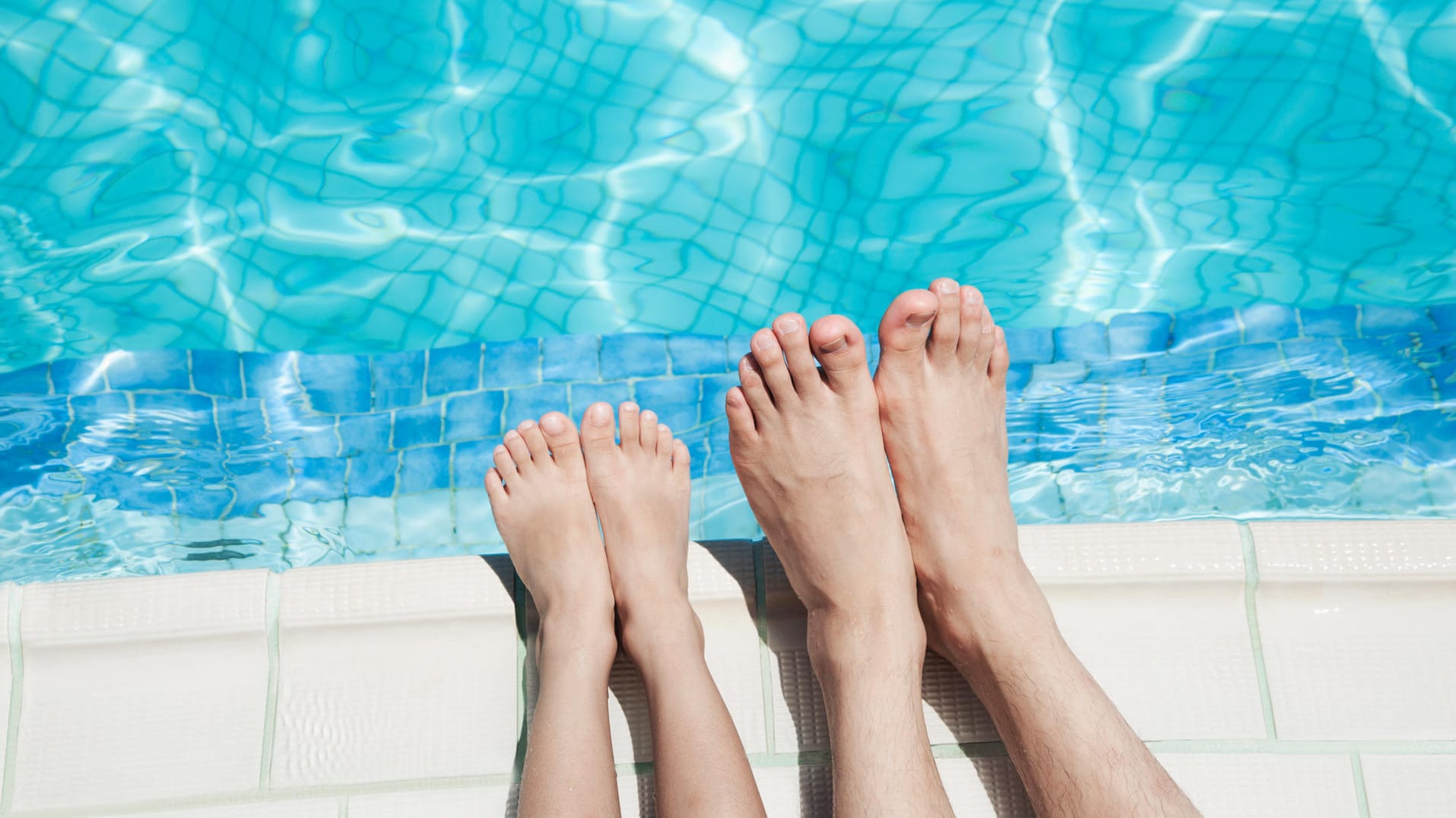 Füße eines Kindes und einer Erwachsenen am Rand eines Schwimmbeckens.