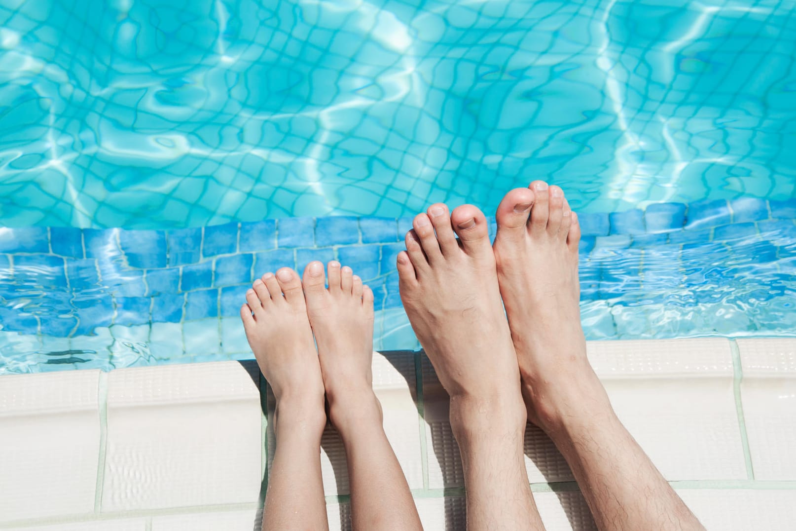 Füße eines Kindes und einer Erwachsenen am Rand eines Schwimmbeckens.