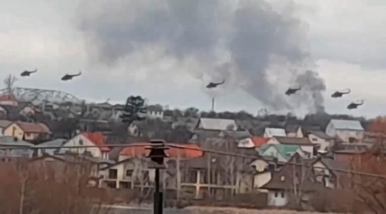 Auf diesem Foto fliegen offenbar russische Militärhubschrauber über einen Vorort von Kiew, während am Horizont Rauch aufsteigt.