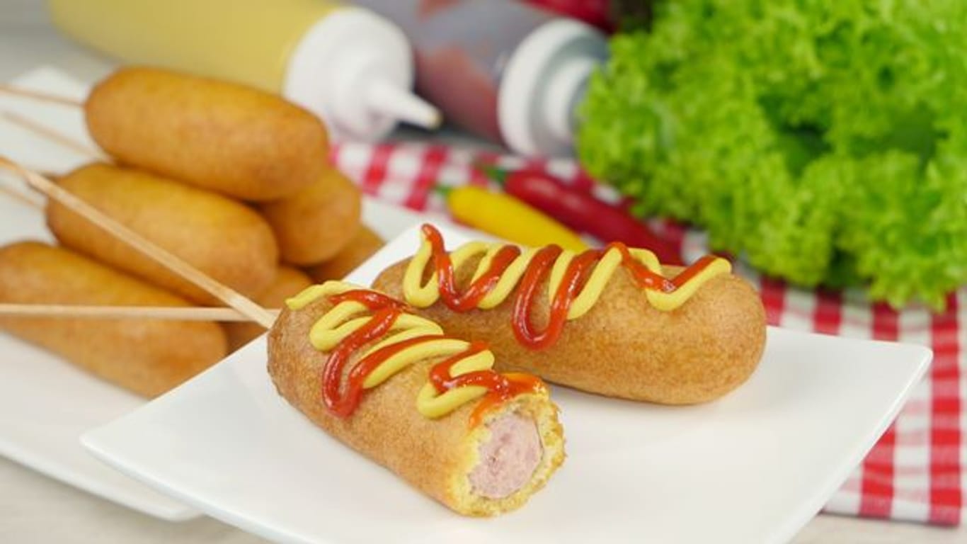Klassische Corn Dogs bestehen aus aufgespießten Hot-Dog-Würstchen in einer Maisteighülle.