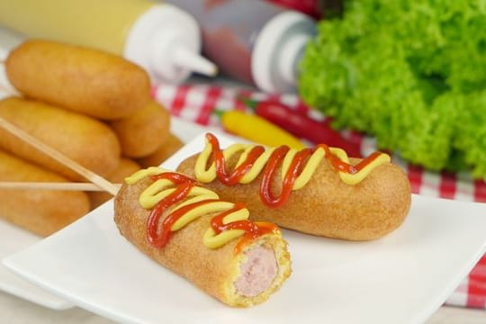 Klassische Corn Dogs bestehen aus aufgespießten Hot-Dog-Würstchen in einer Maisteighülle.