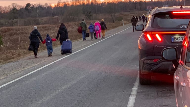 Frauen gehen zu Fuß an einer Autoschlange vorbei: Der Stau vor den Grenzübergängen ist laut Aussagen von Geflüchteten mittlerweile 30 bis 40 Kilometer lang.