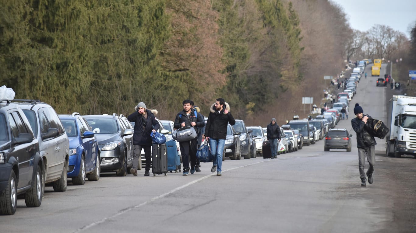 Ukraine, Shehyni: Menschen gehen an einer Schlange von Autos vorbei, die auf dem Weg zur polnischen Grenze sind.