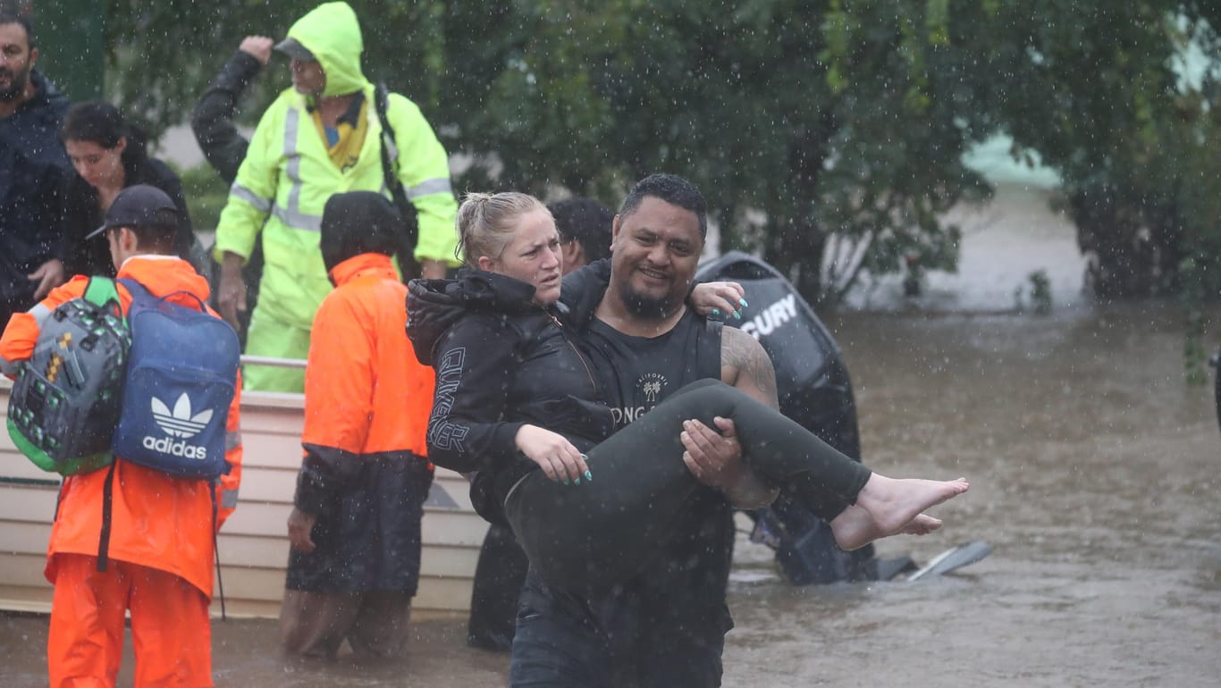 Ein Mann rettet eine junge Frau aus den Fluten: In Australien gab es bislang zehn Todesopfer nach Überschwemmungen.