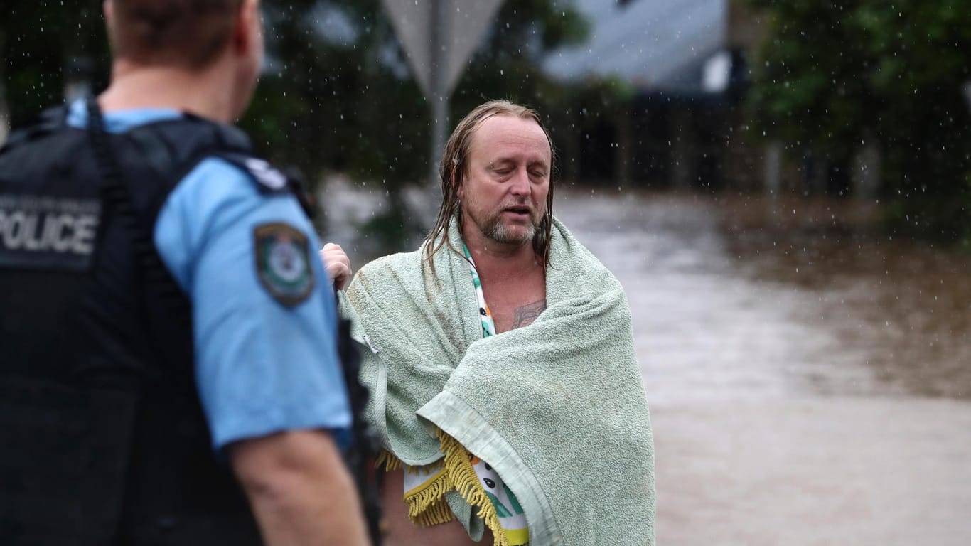 Ein Mann ist in eine Decke eingewickelt, um sich vor dem Regen zu schützen. Sintflutartiger Regen hat die schweren Überschwemmungen im Osten Australiens weiter verschärft.