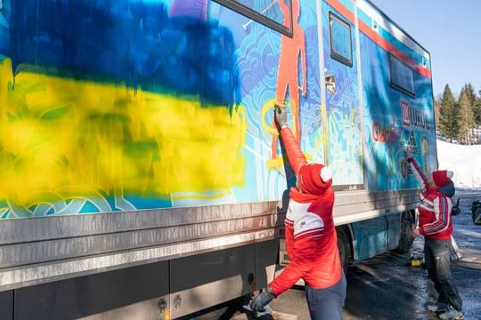 Mitglieder der russischen Langlauf-Nationalmannschaft versuchen, eine ukrainische Flagge und den Schriftzug "Ruhm für die Ukraine" zu entfernen.