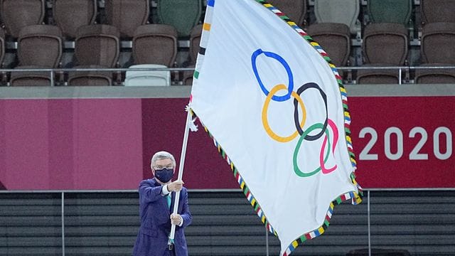 IOC-Präsident Thomas Bach hält die Fahne olympische Fahne hoch.