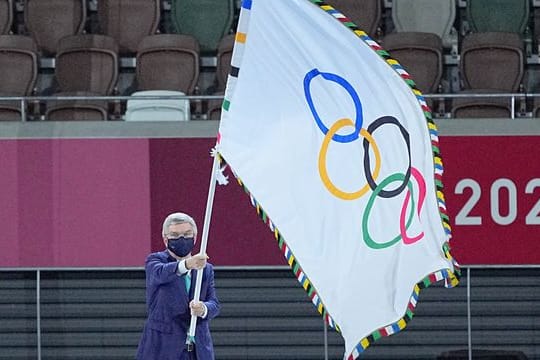 IOC-Präsident Thomas Bach hält die Fahne olympische Fahne hoch.