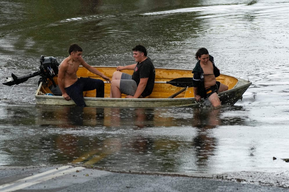 Menschen fahren in einem Boot auf einer überfluteten Straße: In Australien ist es zu Überschwemmungen gekommen.