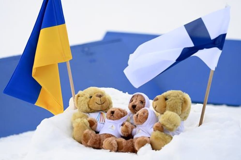 Fahnen der Ukraine und Finnlands in Kontiolahti neben den Weltcup-Maskottchen im Schnee.
