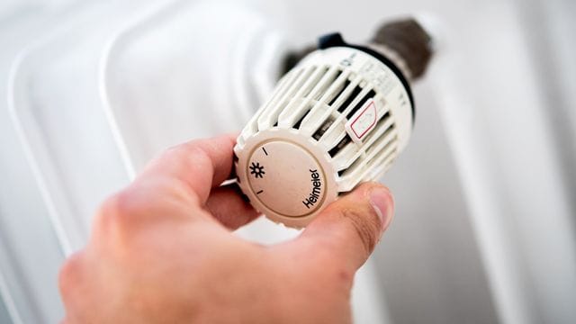 Ein Mann dreht in einer Wohnung am Thermostat einer Heizung Ein Mann dreht in einer Wohnung am Thermostat einer Heizung