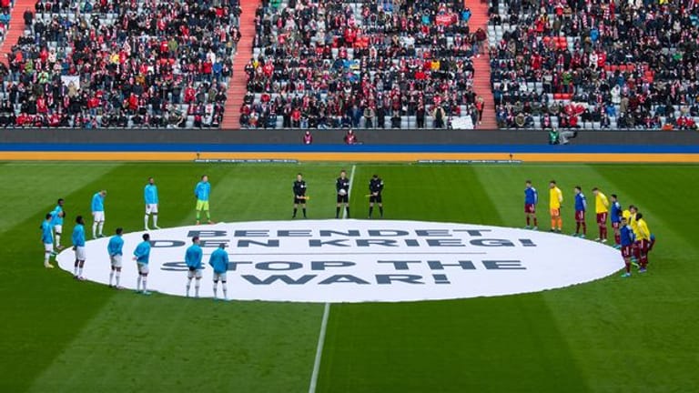 Die Spieler von München und von Leverkusen stehen um ein Banner mit "Beendet den Krieg! - Stop the War!".