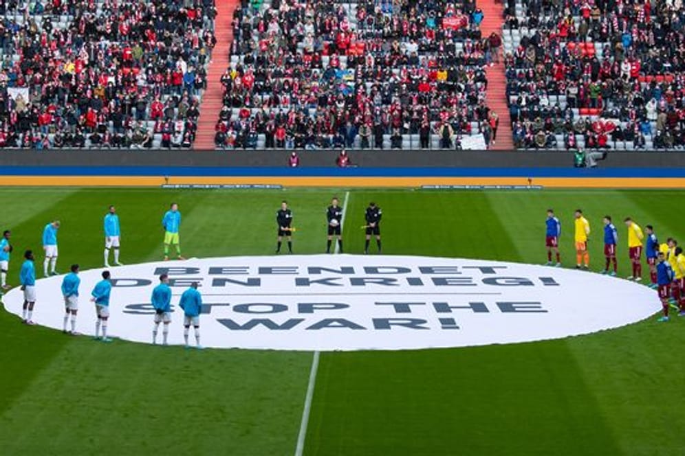 Die Spieler von München und von Leverkusen stehen um ein Banner mit "Beendet den Krieg! - Stop the War!".