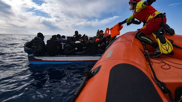 Mitglieder der NGO Open Arms helfen Migranten, die in einem Holzboot vor der Küste Libyens im Mittelmeer aufgebrochen sind.