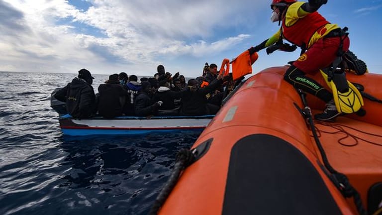 Mitglieder der NGO Open Arms helfen Migranten, die in einem Holzboot vor der Küste Libyens im Mittelmeer aufgebrochen sind.