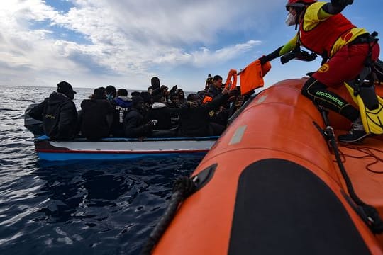 Mitglieder der NGO Open Arms helfen Migranten, die in einem Holzboot vor der Küste Libyens im Mittelmeer aufgebrochen sind.