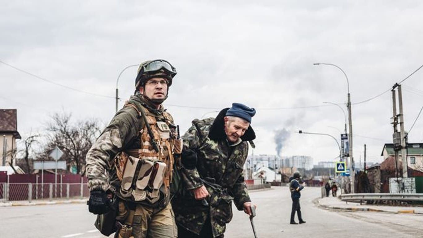 Ein ukrainischer Soldat hilft einem älteren Mann, die Straße zu überqueren.