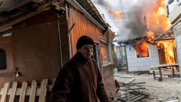 24 Kilometer von Kiew entfernt steht ein Einwohner vor einem brennenden Wohnhaus.