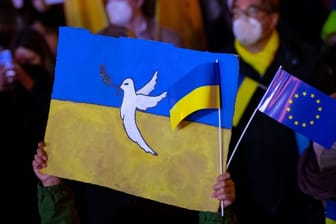 In München hält ein Kind Schilder mit einer Friedenstaube und der Flagge der Ukraine in die Höhe.