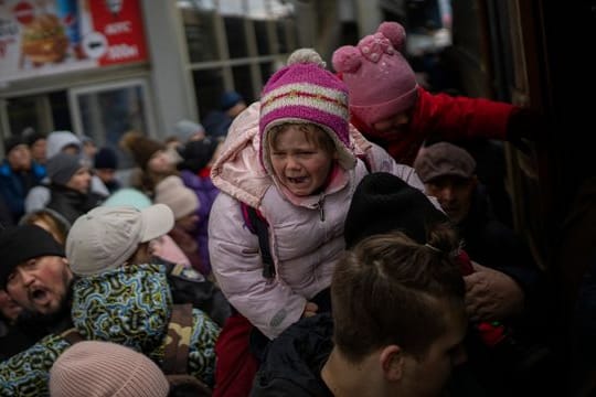 Menschen tragen ihre Kinder und versuchen am Bahnhof von Kiew, in einen Zug nach Lwiw zu steigen.
