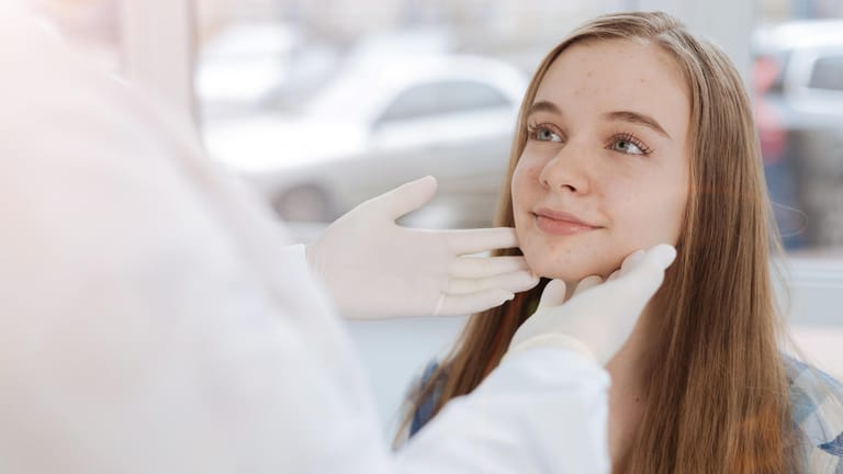 Eine Ärztin schaut sich die Gesichtshaut einer Jugendlichen an.