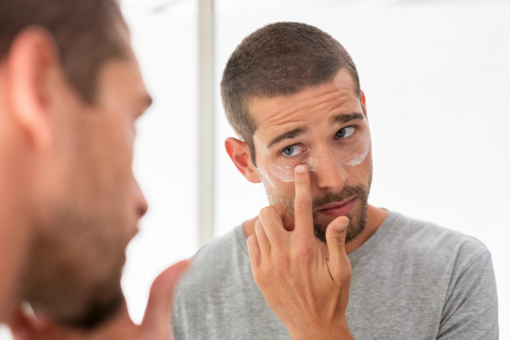 Ein Mann cremt sich die Haut unter den Augen ein.