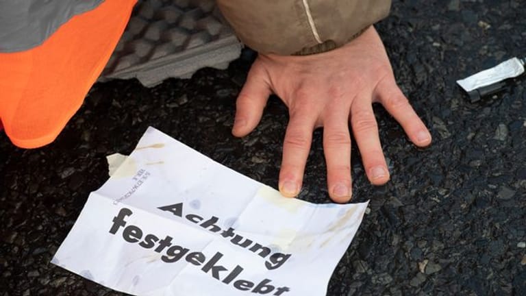"Achtung festgeklebt" steht auf dem Zettel eines Demonstranten (Archivbild): Nach den Autobahn-Blockaden kommen mehrere hundert Anzeigen auf die Klimaaktivisten zu.