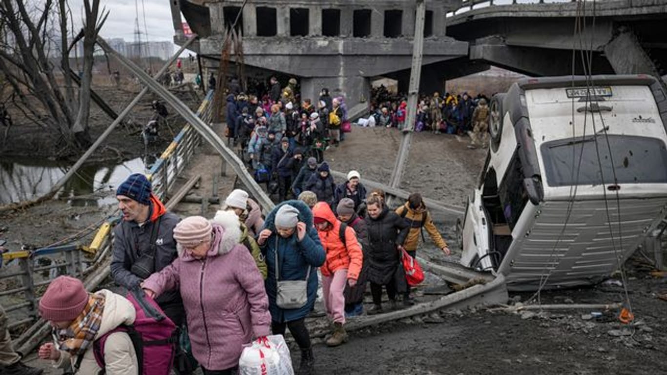 Menschen aus der Ukraine überqueren den Fluss Irpin auf einem improvisierten Weg unter einer zerstörten Brücke.
