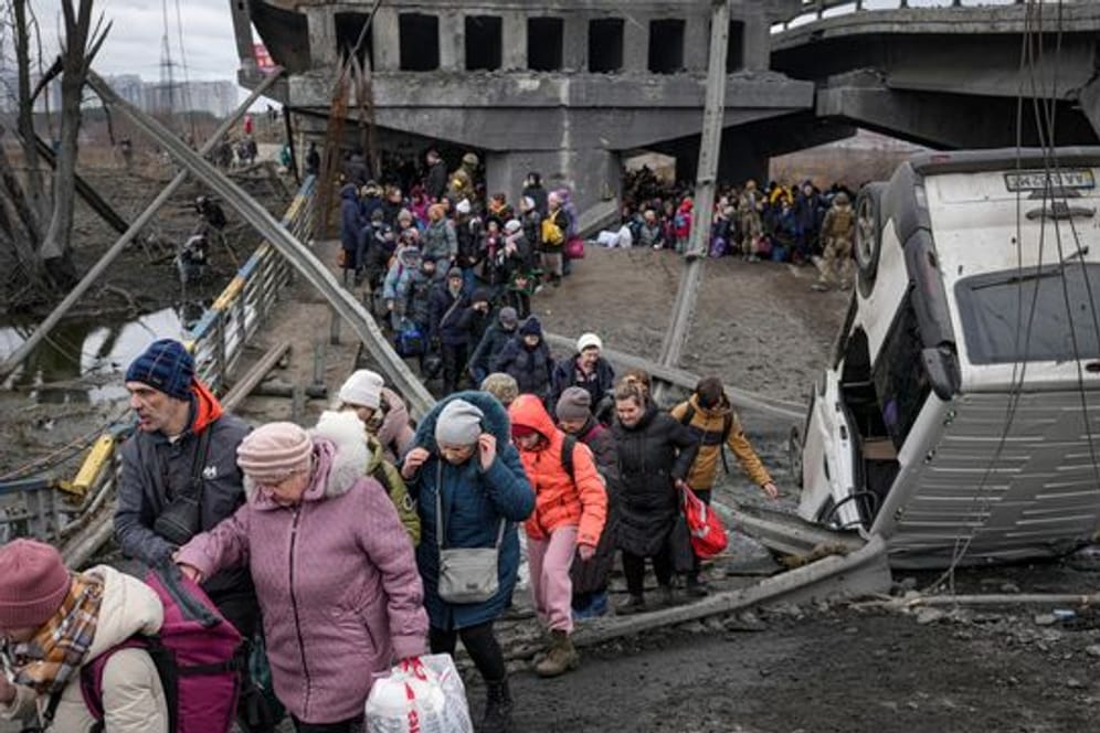 Menschen aus der Ukraine überqueren den Fluss Irpin auf einem improvisierten Weg unter einer zerstörten Brücke.