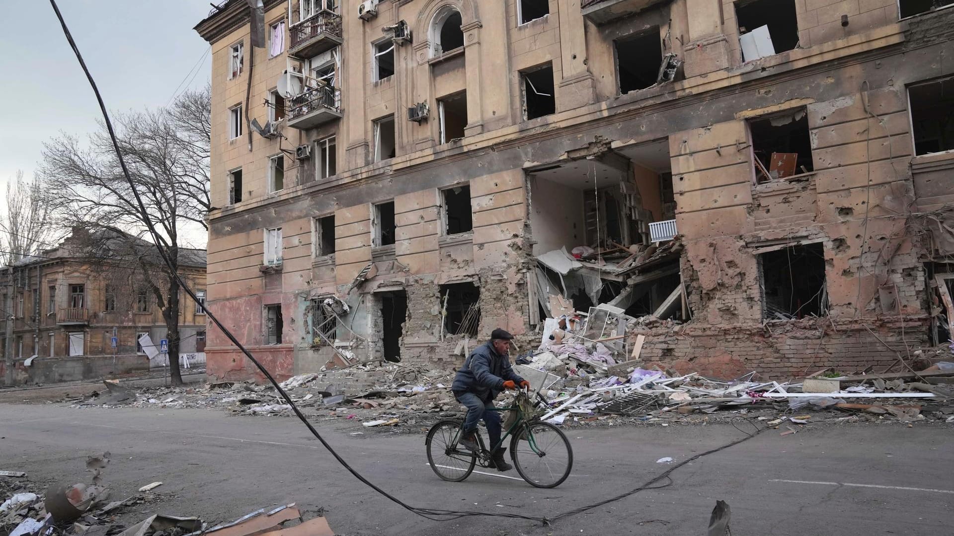 Ein Mann fährt mit dem Fahrrad an einem durch einen Angriff beschädigten Wohnhaus in Mariupol vorbei.