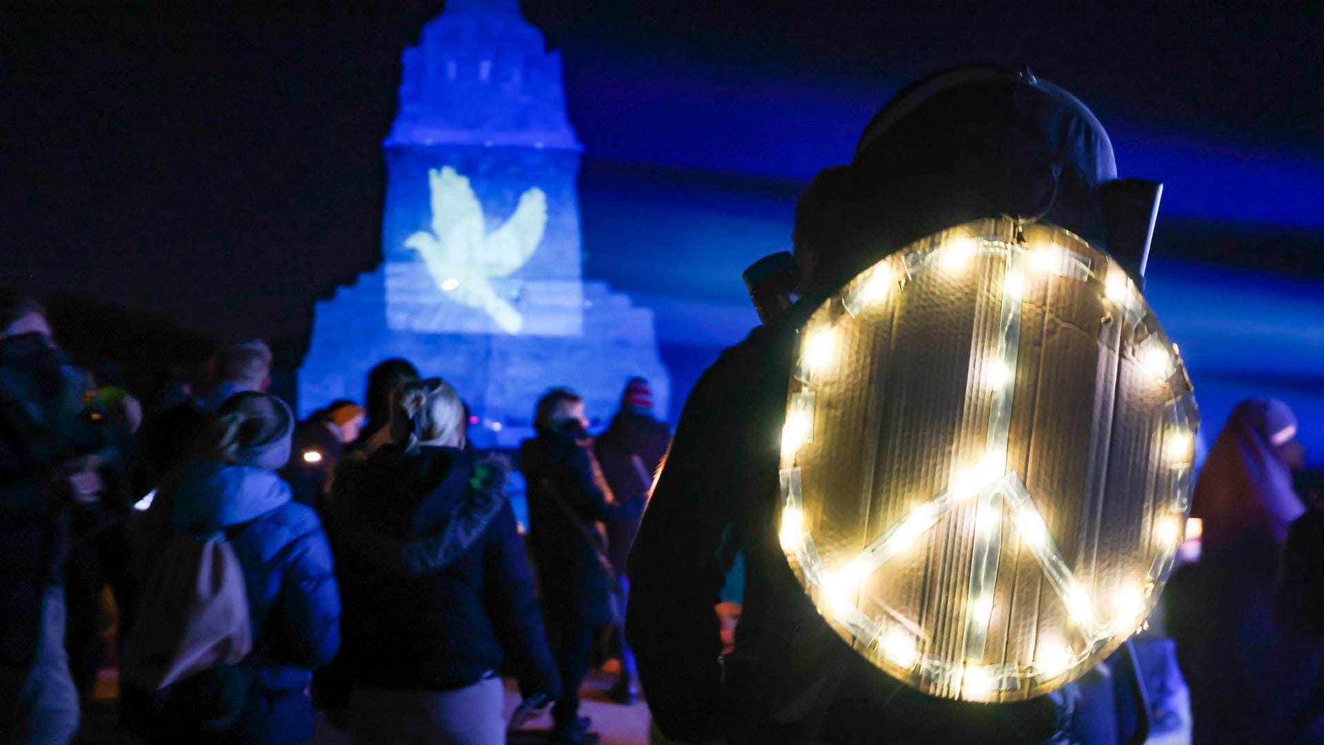 Aktion in Leipzig: Ein Mann steht mit einem leuchtenden Peace-Zeichen auf dem Rücken vor dem Völkerschlachtdenkmal.