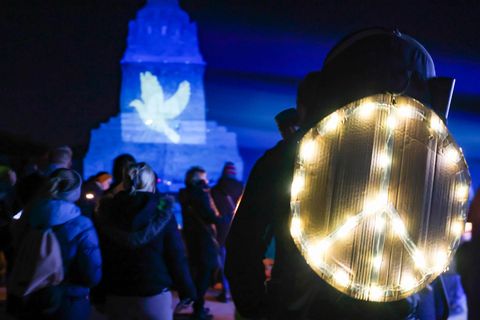 Aktion in Leipzig: Ein Mann steht mit einem leuchtenden Peace-Zeichen auf dem Rücken vor dem Völkerschlachtdenkmal.