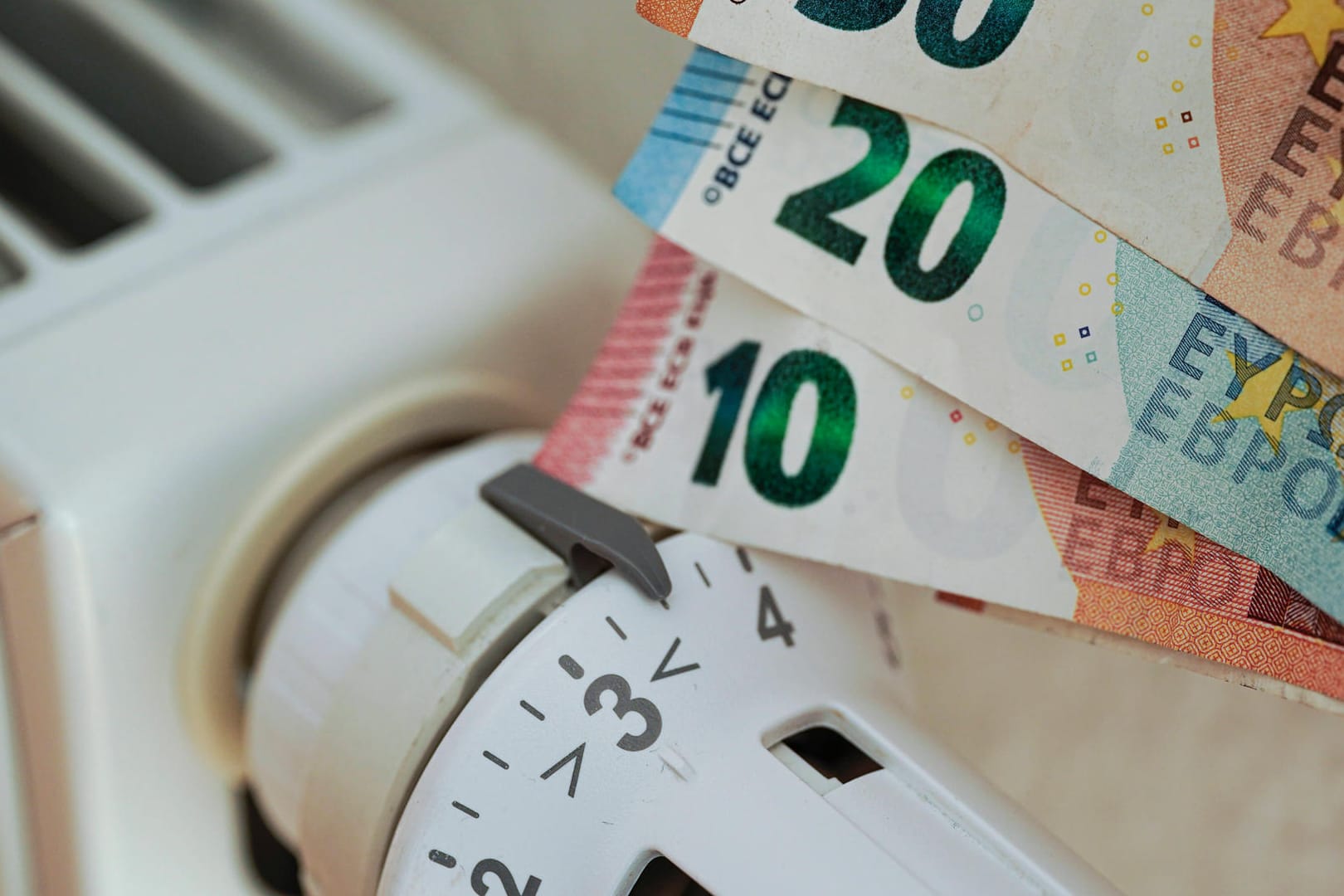 Bargeld neben einer aufgedrehten Heizung (Symbolbild): Die hohen Heizkosten stellen eine finanzielle Belastung dar.