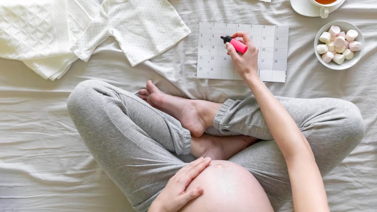 Blick von oben: Eine Schwangere markiert etwas im Kalender.