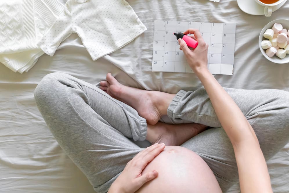 Blick von oben: Eine Schwangere markiert etwas im Kalender.