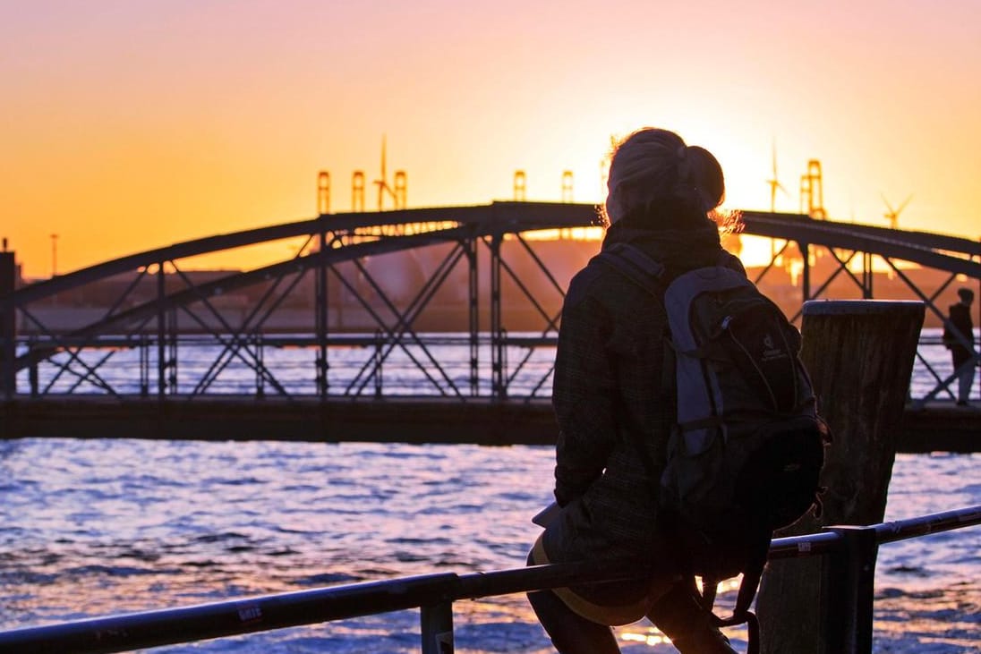 Eine Frau sitzt bei Sonnenuntergang an der Norderelbe am Hamburger Hafen (Archivbild): Im Norden wird ein sonniges und windiges Wochenende erwartet.