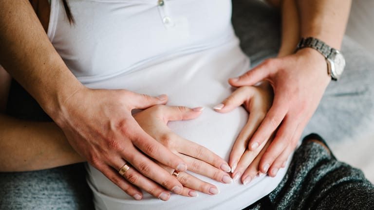 Mann und Frau halten ihre Hände auf den Babybauch der Frau.
