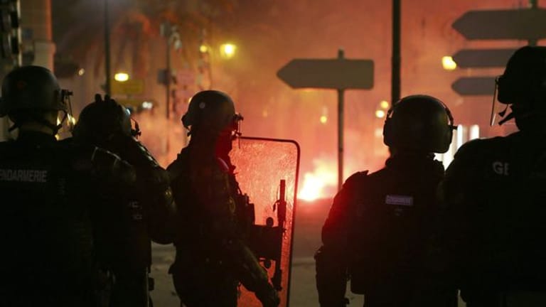 Französische Gendarmen stehen auf der Straße in Ajaccio auf Korsika, während es im Hintergrund brennt.