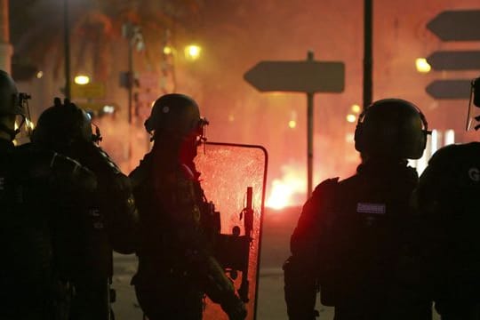 Französische Gendarmen stehen auf der Straße in Ajaccio auf Korsika, während es im Hintergrund brennt.