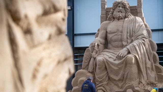 Ein Mann arbeitet an einer Sandskulptur des Göttervaters Zeus auf seinem Thron. Ein Mann arbeitet an einer Sandskulptur des Göttervaters Zeus auf seinem Thron.