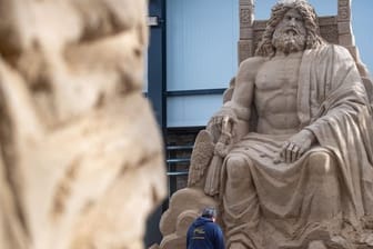 Ein Mann arbeitet an einer Sandskulptur des Göttervaters Zeus auf seinem Thron.