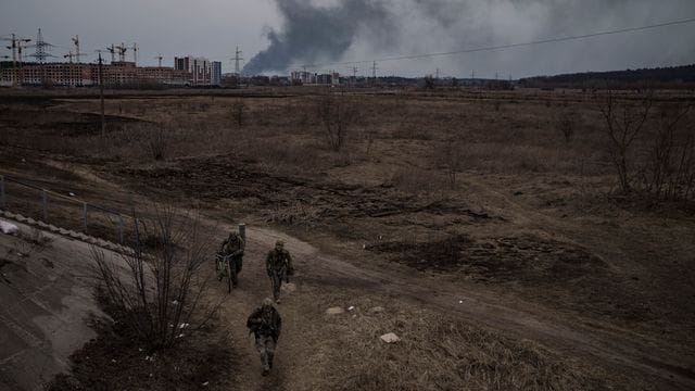 Soldaten gehen einen Weg entlang, während Rauch in Irpin nordwestlich von Kiew aufsteigt.