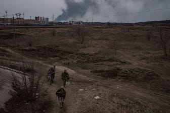 Soldaten gehen einen Weg entlang, während Rauch in Irpin nordwestlich von Kiew aufsteigt.